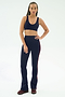 A person faces forward, wearing the SPLITS59 Raquel High Waist Flared Legging in Indigo/Dark Cherry and a navy sports bra, paired with burgundy sneakers against a plain white background.
