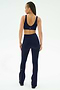A woman with her back to the camera wears SPLITS59’s Raquel High Waist Flared Legging in Indigo/Dark Cherry and a matching navy spandex sports bra, both crafted from soft nylon, set against a plain white background.