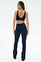 A woman with her back to the camera wears SPLITS59’s Raquel High Waist Flared Legging in Indigo/Dark Cherry and a matching navy spandex sports bra, both crafted from soft nylon, set against a plain white background.