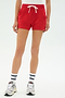 Model wears the SPLITS59 Reena Sweatshort in Pirate Red, paired with white sneakers, blue-striped white athletic socks, and a white top, standing against a plain light background.