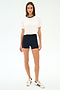 A woman faces forward against a white background, wearing the SPLITS59 Djuna Crop Ringer in White/Indigo, black high-waisted shorts, and white sneakers with black stripes.