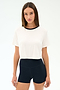 A woman faces forward in the SPLITS59 Djuna Crop Ringer - White/Indigo and high-waisted black shorts, ready for gym workouts or CrossFit, against a plain light background.