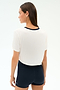 A woman faces away against a plain light background, ready for the gym in the SPLITS59 Djuna Crop Ringer - White/Indigo and black high-waisted shorts.