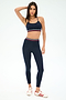 A woman poses against a white background in SPLITS59's Bailey High Waist Active Rib 7/8 leggings in Heather Indigo and a matching sports bra with striped bands, paired with white sneakers featuring red stripes.