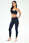 A woman wears the SPLITS59 Bailey High Waist Active Rib 7/8 leggings in Heather Indigo with a matching sports bra, both featuring red, white, and blue stripes, paired with white Adidas sneakers.