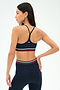 A woman poses from the back against a plain background, wearing the SPLITS59 Cali Active Rib Bra in Heather Indigo and matching high-waisted leggings with red, white, and navy striped bands.