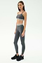 A woman stands against a plain background wearing the SPLITS59 Cali Active Rib Bra in Heather Grey with matching leggings featuring white striped bands, and black sneakers.