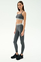 A woman stands against a plain background wearing the SPLITS59 Cali Active Rib Bra in Heather Grey with matching leggings featuring white striped bands, and black sneakers.