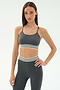 A woman in the SPLITS59 Cali Active Rib Bra in Heather Grey stands against a plain light background, paired with matching high-waisted leggings featuring white and black stripes.