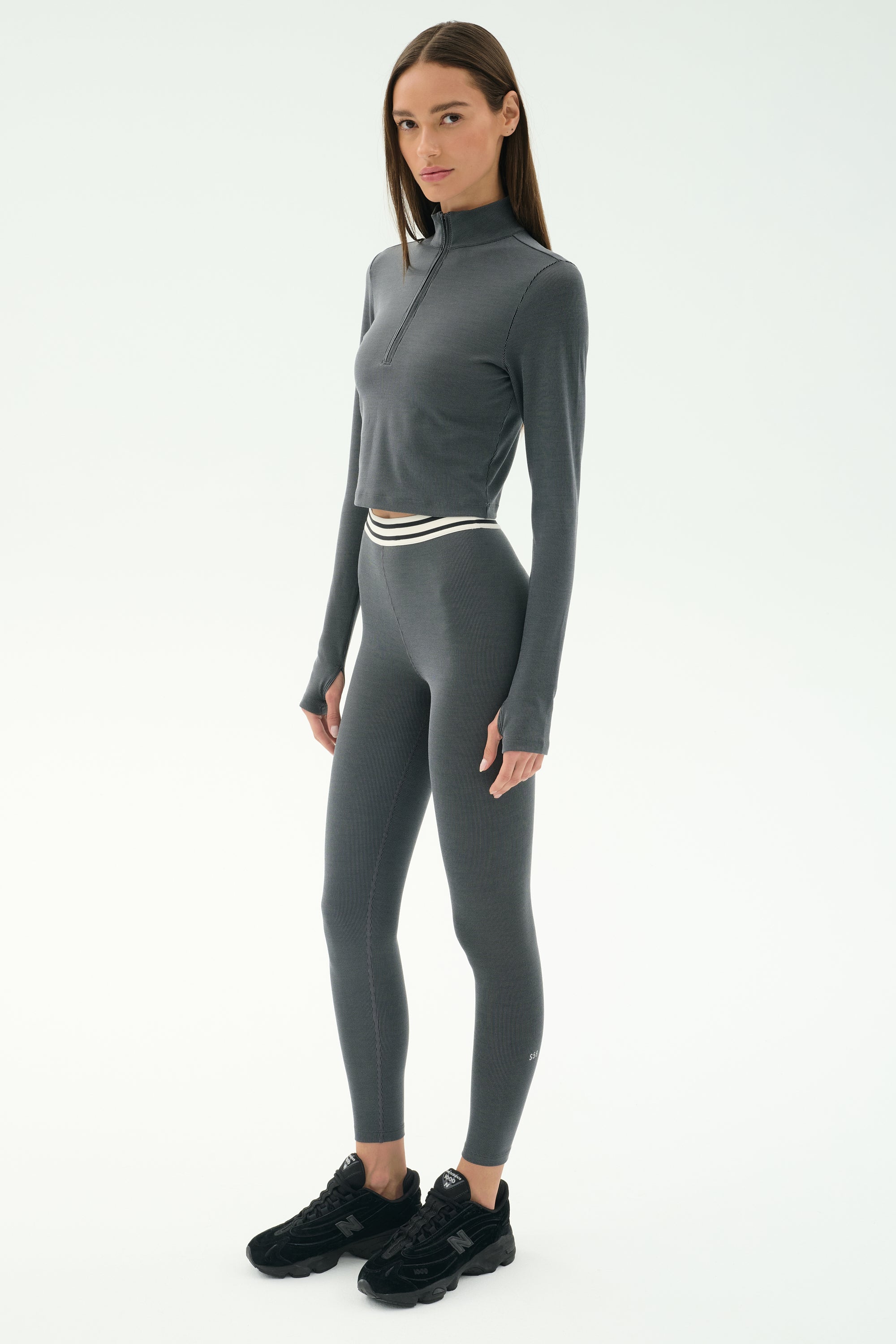 A woman models the SPLITS59 Stevie Active Rib Half Zip in Heather Grey, a fitted long-sleeve activewear top, paired with black sneakers, ready for gym workouts against a plain white background.