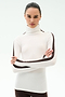 A woman stands with arms crossed, wearing the SPLITS59 Jackson Rib Full Length Turtleneck in White/Dark Chocolate—ideal for yoga or running—against a plain light background.