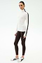 A woman stands against a plain background wearing the SPLITS59 Jackson Rib Full Length Turtleneck in White/Dark Chocolate, brown leggings, and white athletic shoes—ideal for stylish yoga or running sessions.