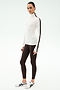 A woman stands against a plain background wearing the SPLITS59 Jackson Rib Full Length Turtleneck in White/Dark Chocolate, brown leggings, and white athletic shoes—ideal for stylish yoga or running sessions.