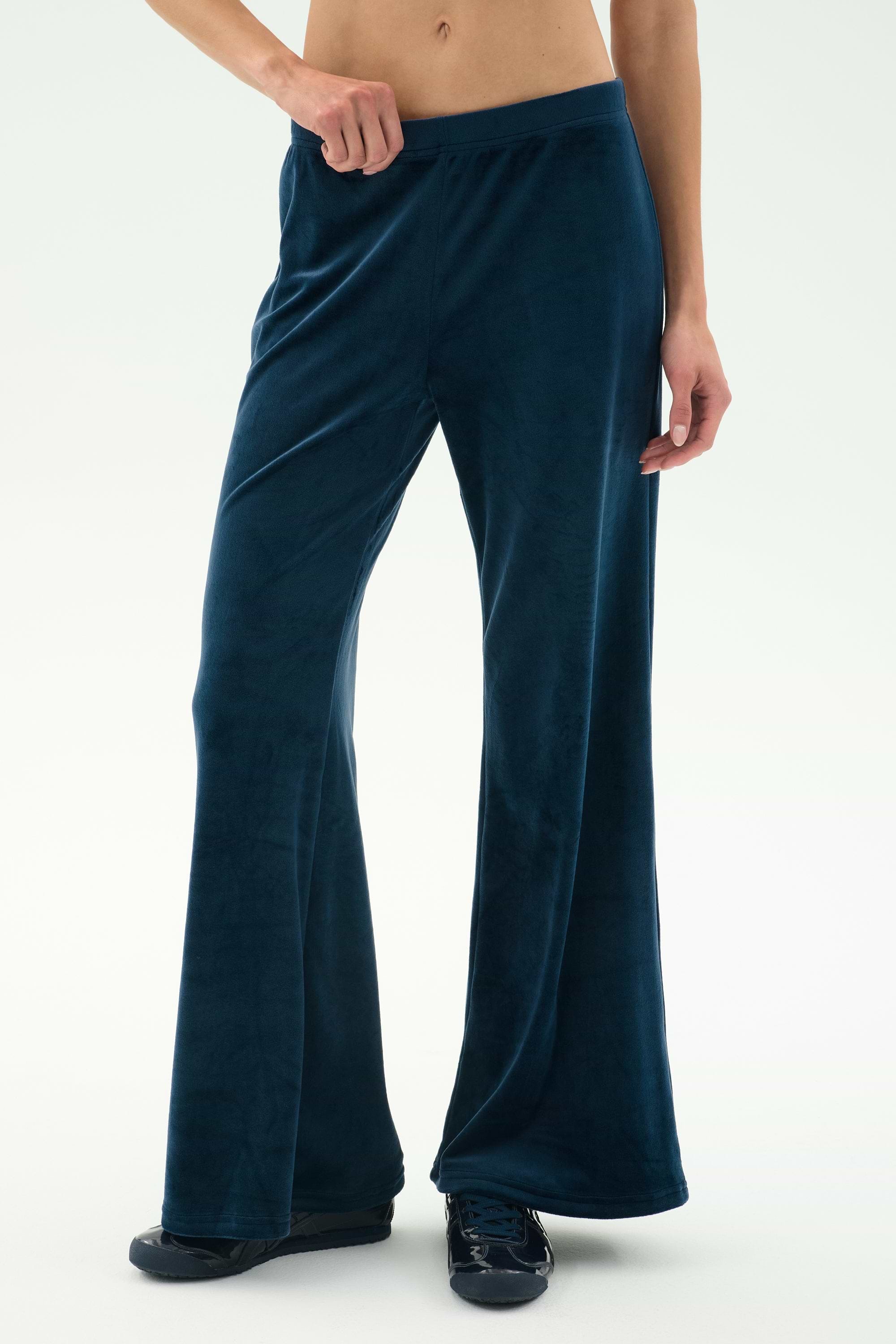 A person wears the SPLITS59 Joy Velour Pant in Indigo with black shoes, standing against a plain light background.