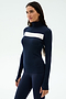 A woman stands against a plain light background wearing the SPLITS59 Lennon Rib Turtleneck in Indigo/White, featuring a fitted silhouette and white horizontal chest stripe, paired with matching navy leggings.