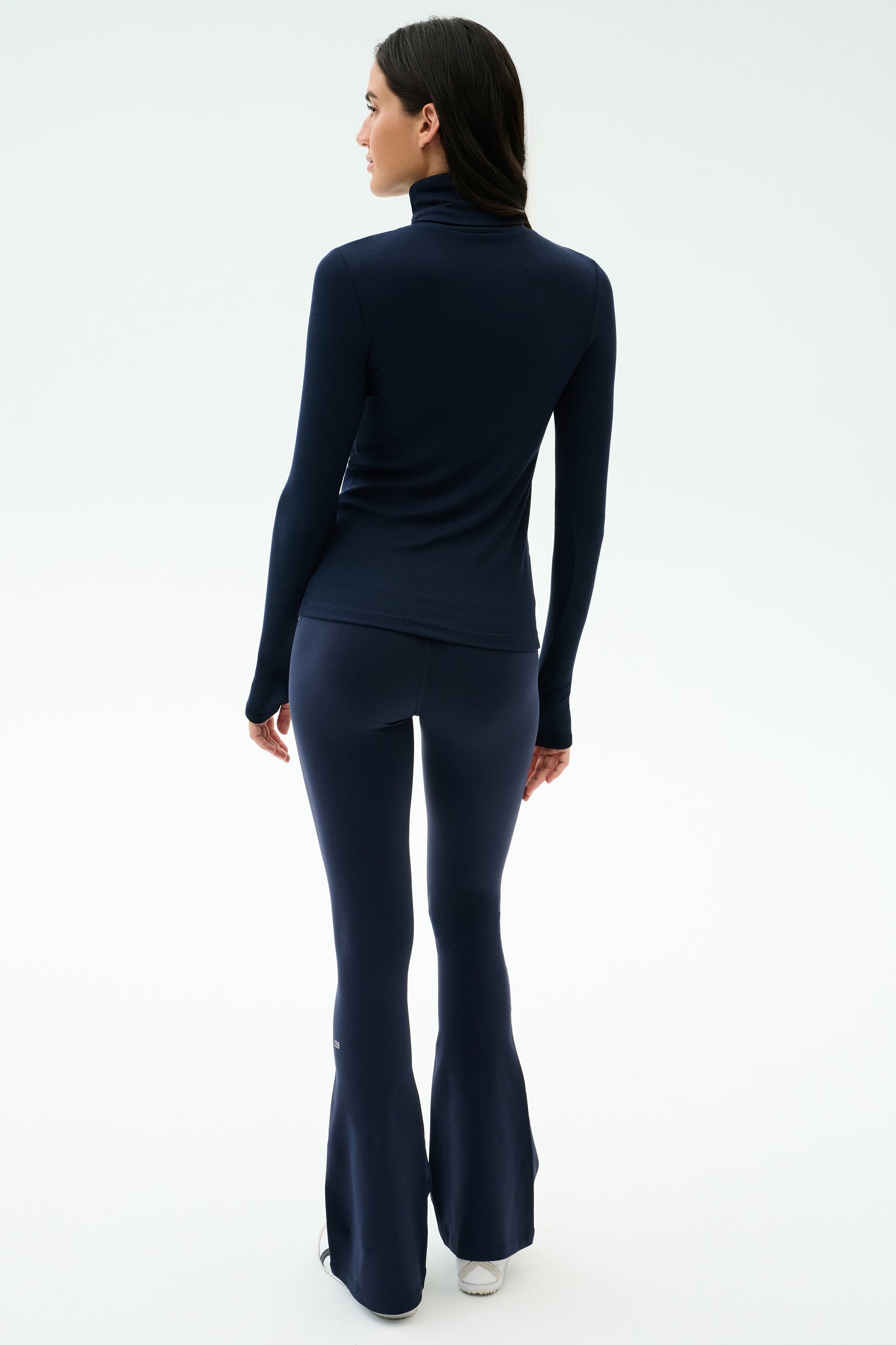A person stands facing away against a plain white background, wearing the SPLITS59 Lennon Rib Turtleneck in Indigo/White with navy flared pants.
