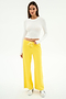 A woman poses against a white background wearing SPLITS59’s Willow Airweight Wide Leg pants in Bright Yellow/White, paired with a long-sleeve white spandex crop top and white sneakers.
