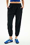 A person wears SPLITS59 Megan Woven Nylon Jogger w/ Piping - Black/Creme, a blue top, and blue athletic shoes, standing with hands in pockets against a plain white background.