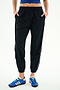 A person wears SPLITS59 Megan Woven Nylon Jogger w/ Piping - Black/Creme, a blue top, and blue athletic shoes, standing with hands in pockets against a plain white background.