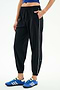 A person stands against a white background wearing SPLITS59 Megan Woven Nylon Jogger w/ Piping - Black/Creme (85% nylon/spandex), featuring a white side stripe, paired with a blue crop top and blue athletic shoes, with one hand in their pocket.