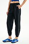 A person stands against a white background wearing SPLITS59 Megan Woven Nylon Jogger w/ Piping - Black/Creme (85% nylon/spandex), featuring a white side stripe, paired with a blue crop top and blue athletic shoes, with one hand in their pocket.