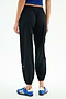 A person wears SPLITS59 Megan Woven Nylon Jogger w/ Piping - Black/Creme, a blue top, and blue athletic shoes, photographed from the back against a plain white background.