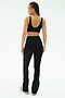 A woman faces away from the camera in SPLITS59’s Raquel High Waist Flared Legging in Black/Creme, paired with a sports bra and sneakers. She poses against a plain white background.