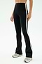 A person stands against a plain white background wearing SPLITS59 Raquel High Waist Flared Legging in Black/Creme, featuring a 4-way stretch, a white side stripe, and light-colored sneakers.