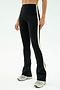 A person stands against a plain white background wearing SPLITS59 Raquel High Waist Flared Legging in Black/Creme, featuring a 4-way stretch, a white side stripe, and light-colored sneakers.
