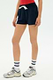 Someone wearing the SPLITS59 Reena Sweatshort in Indigo, a red top, white crew socks, and gray sneakers is standing against a plain white background.