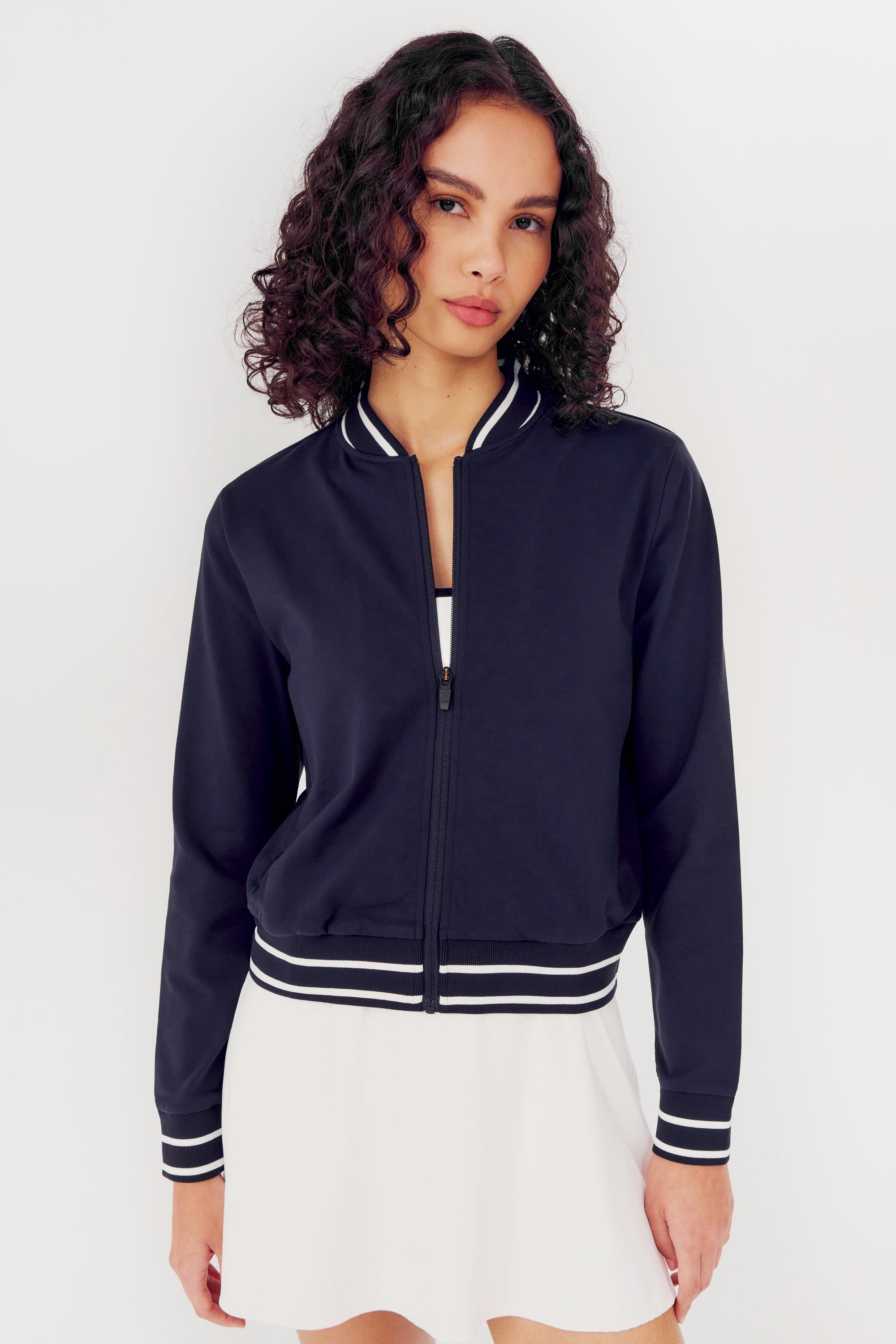 Woman wearing an Ever Supplex Jacket in Indigo by SPLITS59 with white trim and a white spandex skirt.