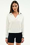 A woman stands against a plain white background wearing the SPLITS59 Taylor Knit Polo in white with black trim and black shorts.