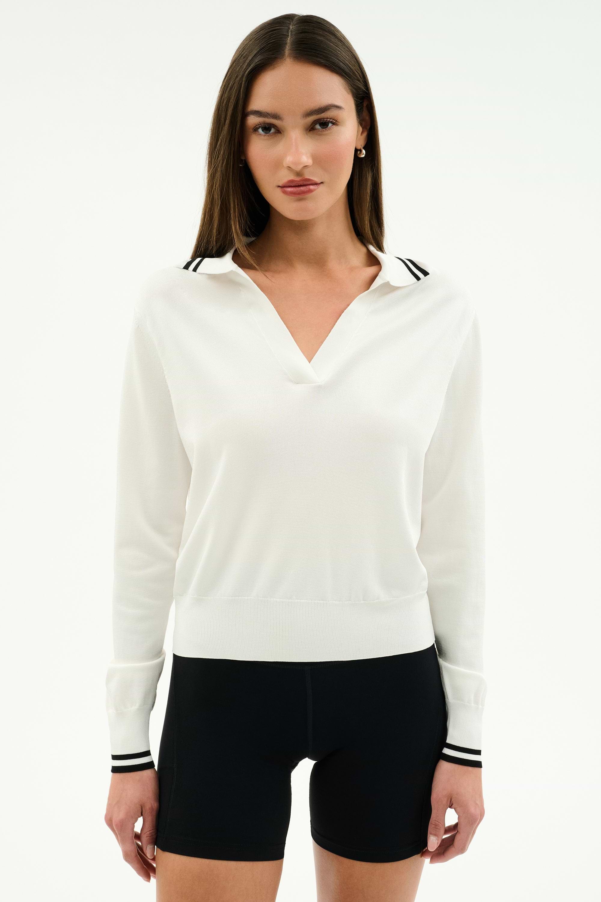 A woman stands against a plain white background wearing the SPLITS59 Taylor Knit Polo in white with black trim and black shorts.
