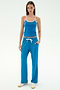 A woman faces forward in the SPLITS59 Airweight Tank - Stone Blue/White, paired with blue drawstring pants with white trim and white sneakers—ideal for hot yoga or Pilates—set against a plain white background.