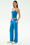 A woman stands against a plain background in the SPLITS59 Airweight Tank—Stone Blue/White—with matching drawstring pants and white sneakers, hands in pockets, ready for Pilates or hot yoga.
