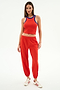 A woman stands against a white background wearing the SPLITS59 Megan Woven Nylon Jogger w/ Piping in Lotus Red/Creme and white sneakers with red stripes.