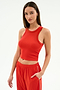 A woman wears the SPLITS59 Kiki Rib Crop Tank in Lotus Red with matching red track pants featuring white trim, standing against a plain white background—ideal for workouts or casual style.