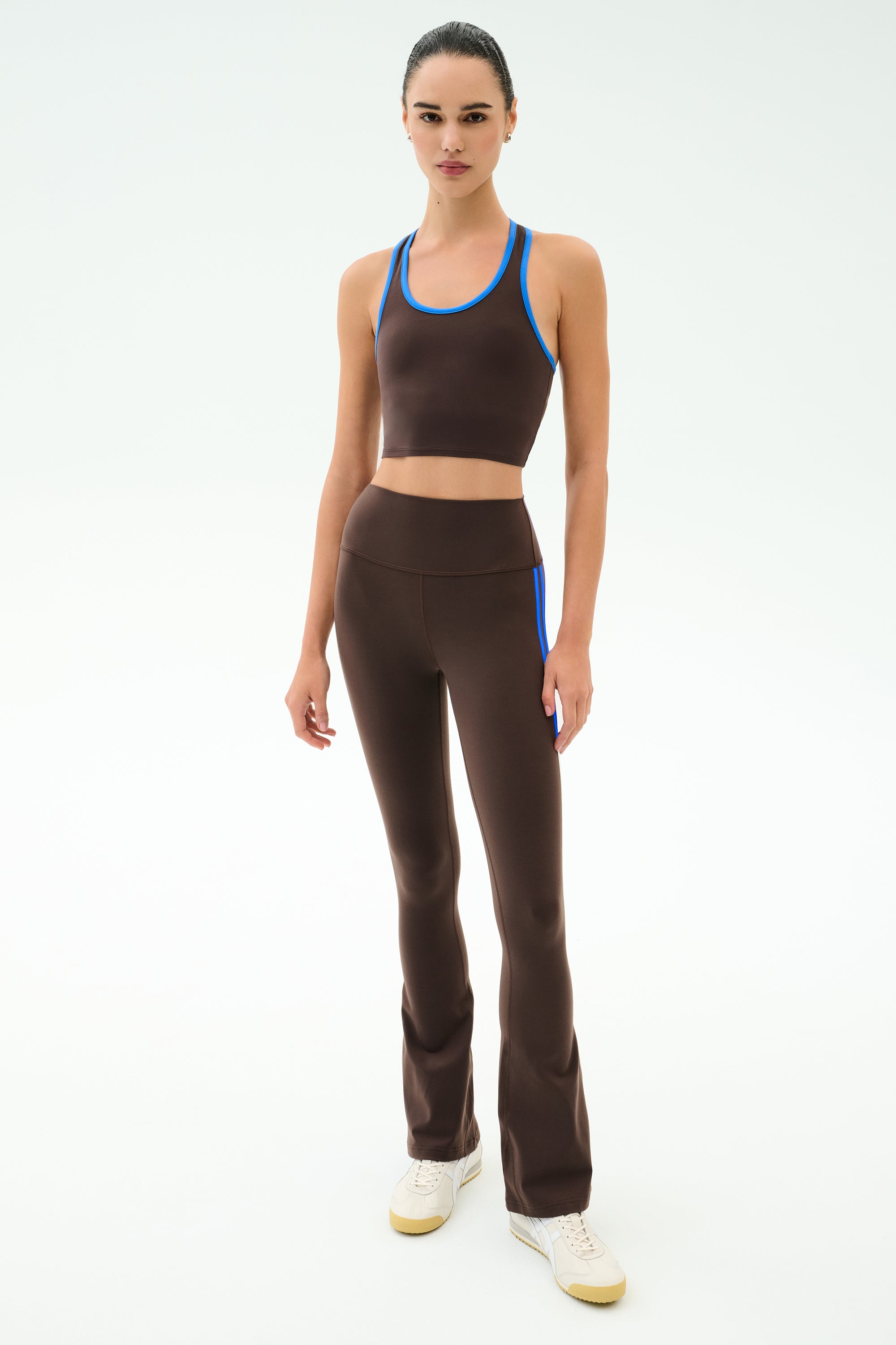 A woman poses in SPLITS59’s Raquel High Waist Supplex Flare in Dark Chocolate/Classic Blue, featuring 4-way stretch supplex—ideal for gym sessions—styled with a matching athletic crop top and white sneakers against a white background.