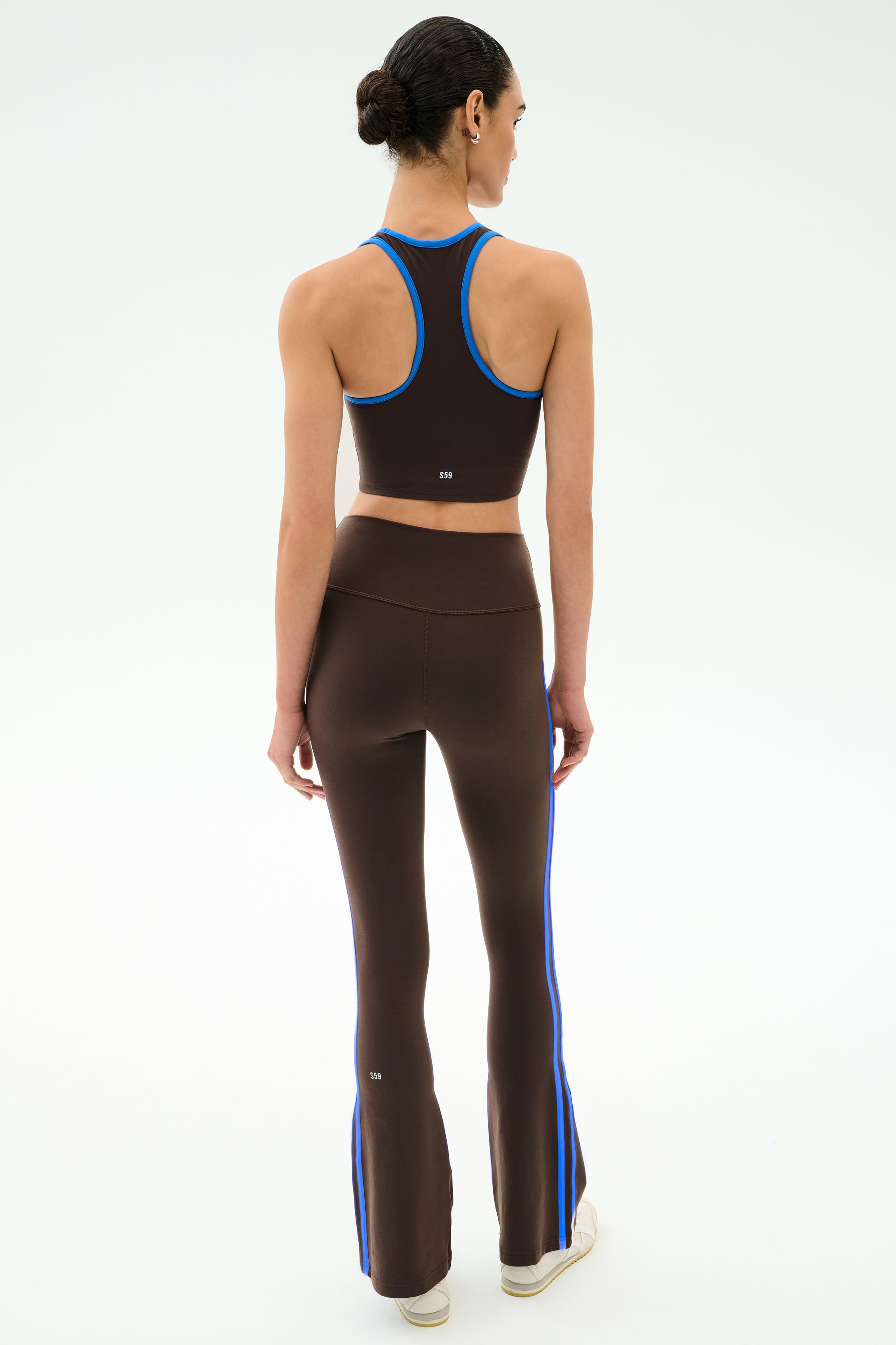 A woman faces away, wearing SPLITS59's Raquel High Waist Supplex Flare leggings in Dark Chocolate/Classic Blue—perfect for gym sessions—against a plain white background.