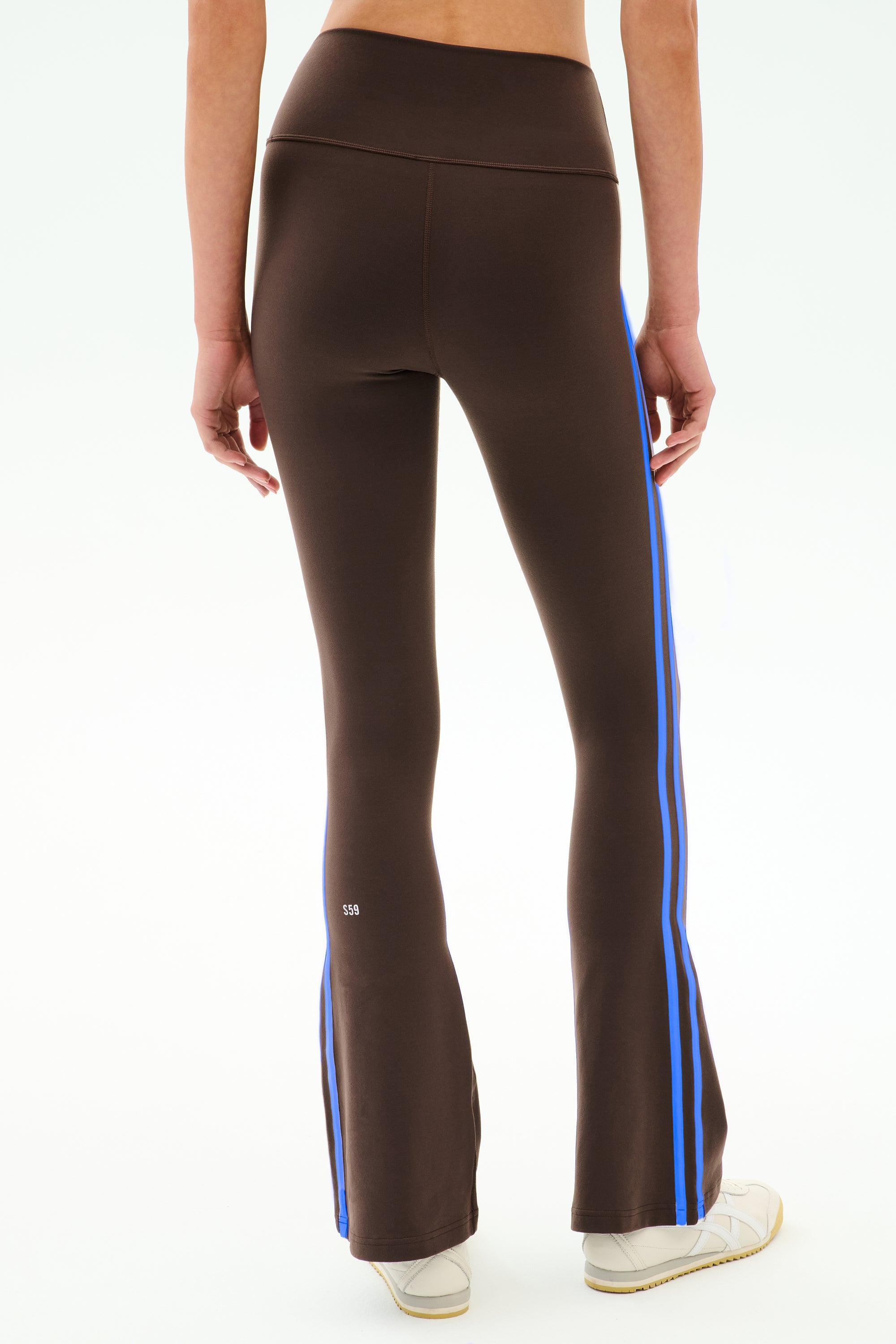 A person wears SPLITS59 Raquel High Waist Supplex Flare leggings in Dark Chocolate/Classic Blue with white sneakers, photographed from the back. Made with 4-way stretch supplex fabric, ideal for gym workouts.