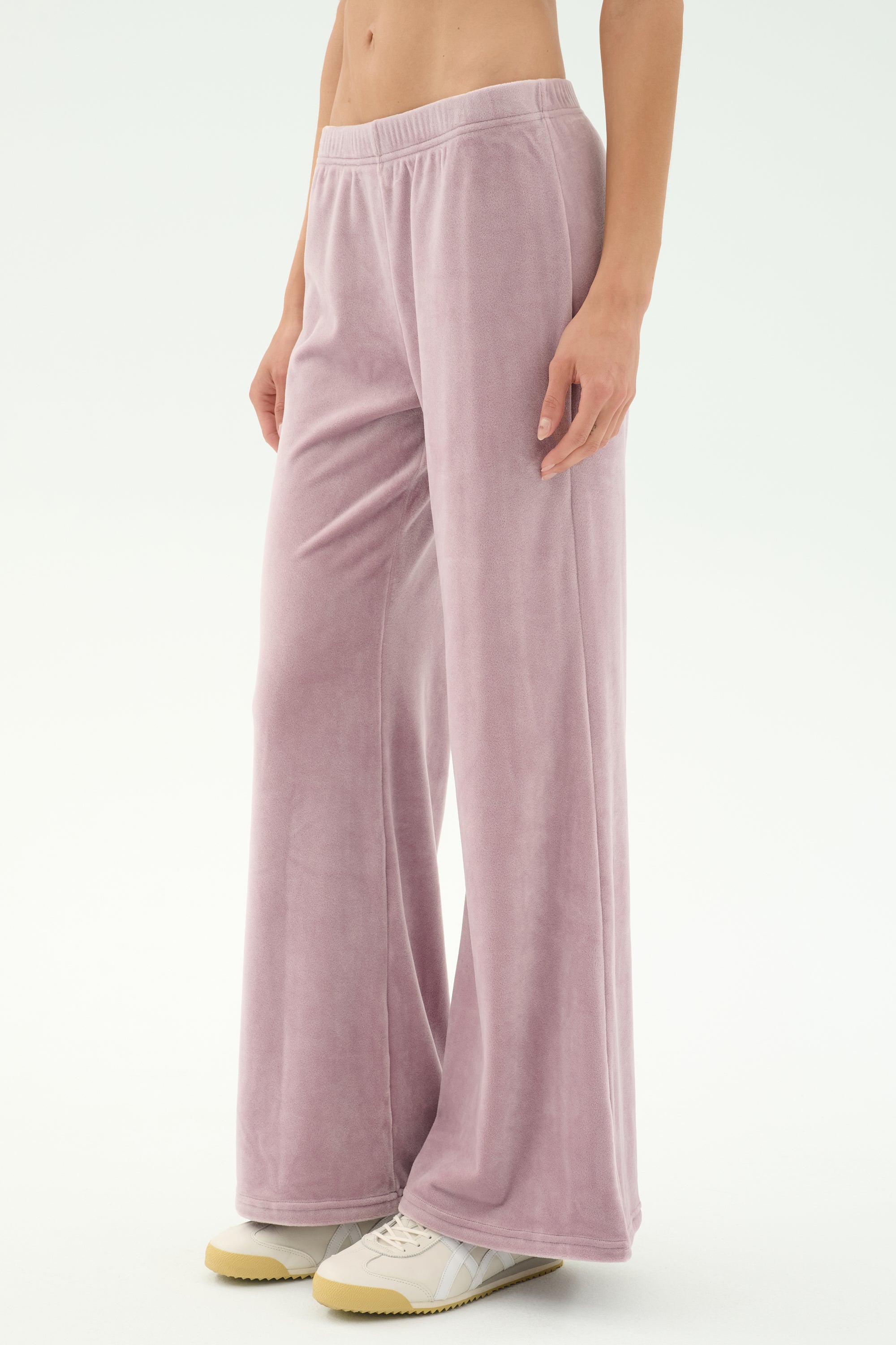 A person stands against a plain background wearing SPLITS59's Joy Velour Pant in Blush and white sneakers.