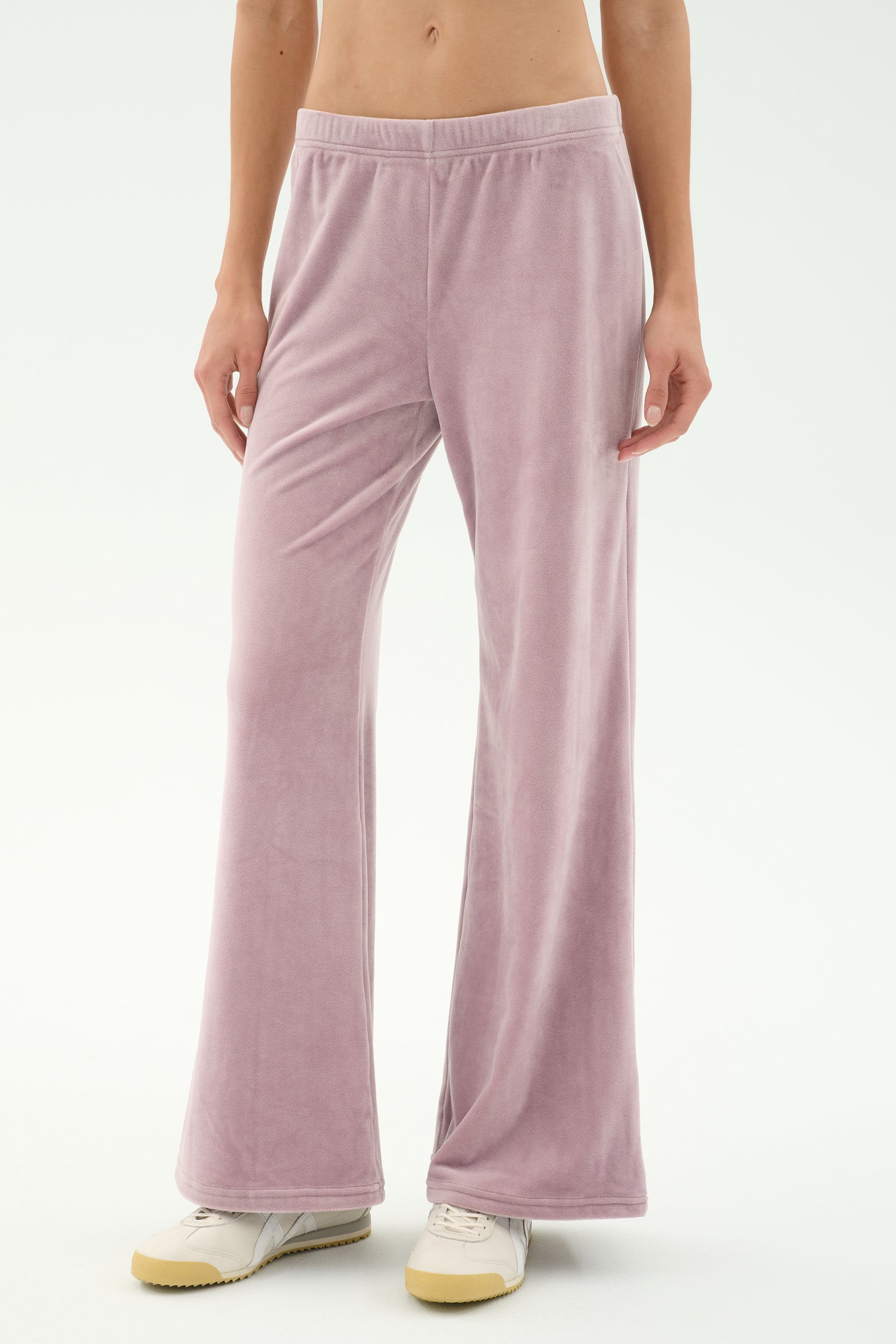 Model wears SPLITS59 Joy Velour Pant in Blush with white sneakers, standing against a plain light background. Upper torso is not visible.
