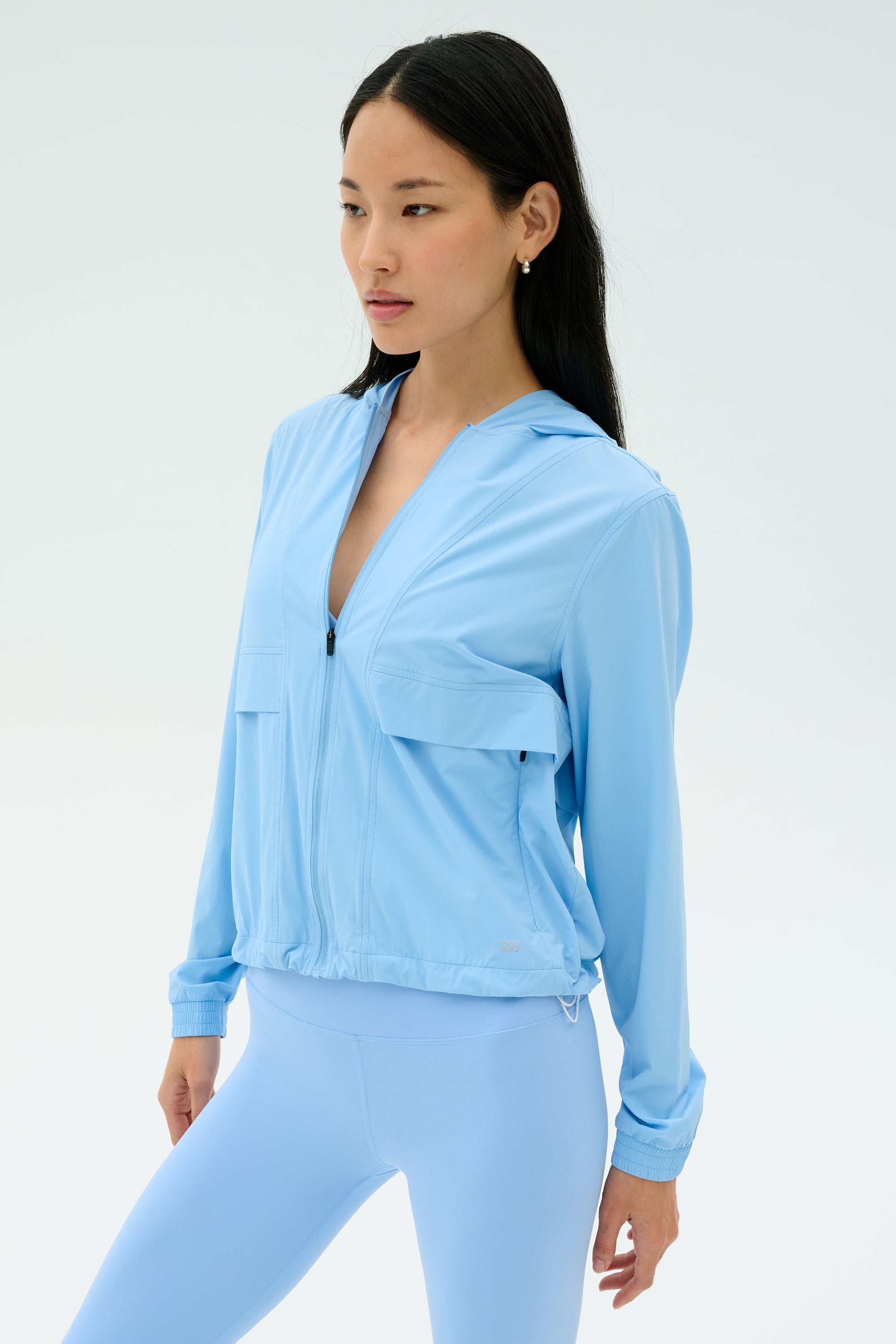 A woman faces slightly left, wearing the SPLITS59 Megan Woven Nylon Jacket in Skylight against a plain, light background.