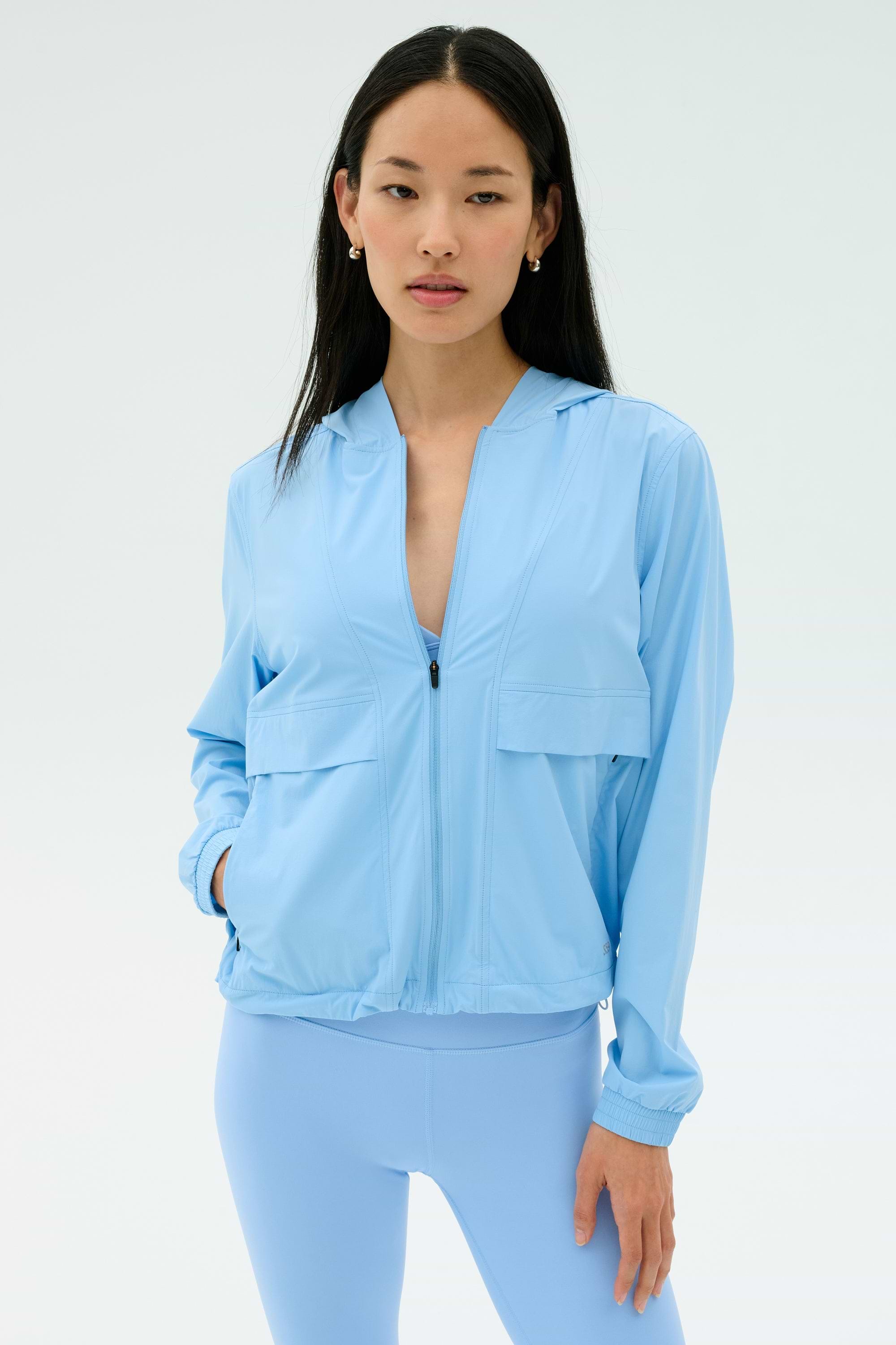 A woman stands against a plain background wearing the SPLITS59 Megan Woven Nylon Jacket in Skylight, with one hand in her pocket.