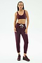 A woman stands against a white background wearing SPLITS59's Reena Fleece 7/8 Sweatpant in Dark Cherry, paired with a matching sports bra and burgundy sneakers.