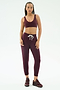 A woman stands against a white background wearing SPLITS59's Reena Fleece 7/8 Sweatpant in Dark Cherry, paired with a matching sports bra and burgundy sneakers.