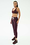 A woman stands against a white background wearing SPLITS59 Reena Fleece 7/8 Sweatpant in Dark Cherry, paired with a matching maroon sports bra and sneakers.