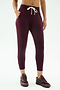 A person models SPLITS59's Reena Fleece 7/8 Sweatpant in Dark Cherry, featuring soft modal with spandex stretch, styled with matching sneakers and a white drawstring, hands in pockets against a plain background.