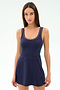 A woman with long brown hair wears the SPLITS59 Martina Rigor Color Block Dress in Indigo/Spearmint, a navy sleeveless athletic style with white trim, made from a stretchy nylon-spandex blend, standing against a plain light background.