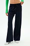 A person wears SPLITS59 Brynn Airweight Pant in Indigo, featuring a comfortable nylon-spandex blend, paired with a green long-sleeve top and white sneakers, standing against a plain white background.